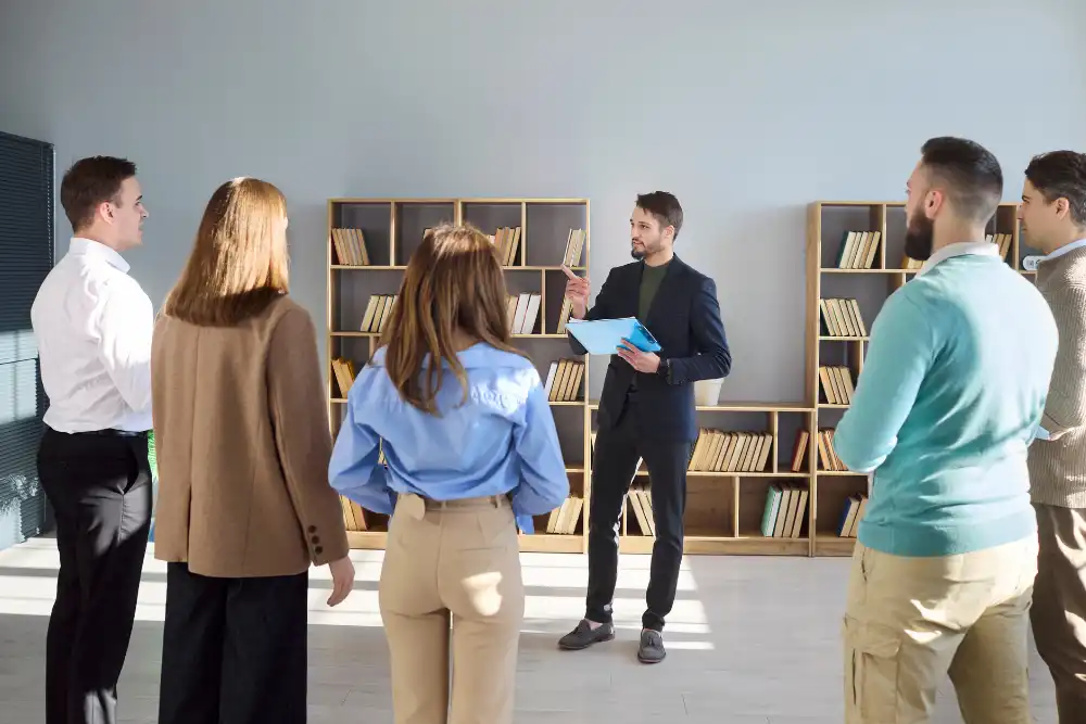 Manager explains a project to colleagues in a bright office while gesturing with a blue folder in hand.