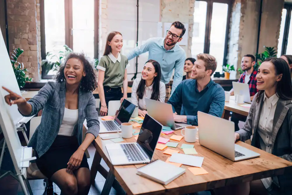 Group of diverse coworkers collaborating around a wooden table with laptops, sticky notes, and coffee cups in a bright office studio.