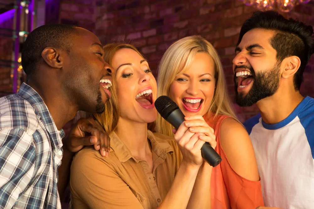 Four friends sing into a microphone together at a karaoke night, smiling and enjoying the moment.